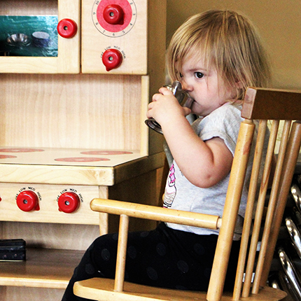 Toddler playing with a play kitchen, drinking out of a pot