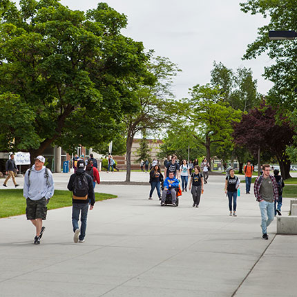 Spokane Falls Community College students walking on the main sidewalk at Spokane Falls Community College. Trees and the library are in the background.